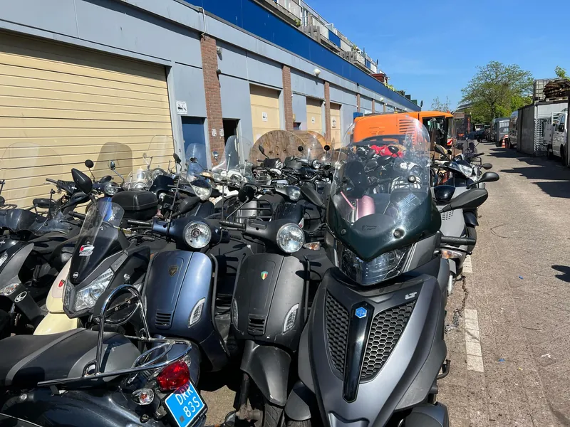 Een rij scooters langs de gevel op de Marktweg, wachtend op hun beurt