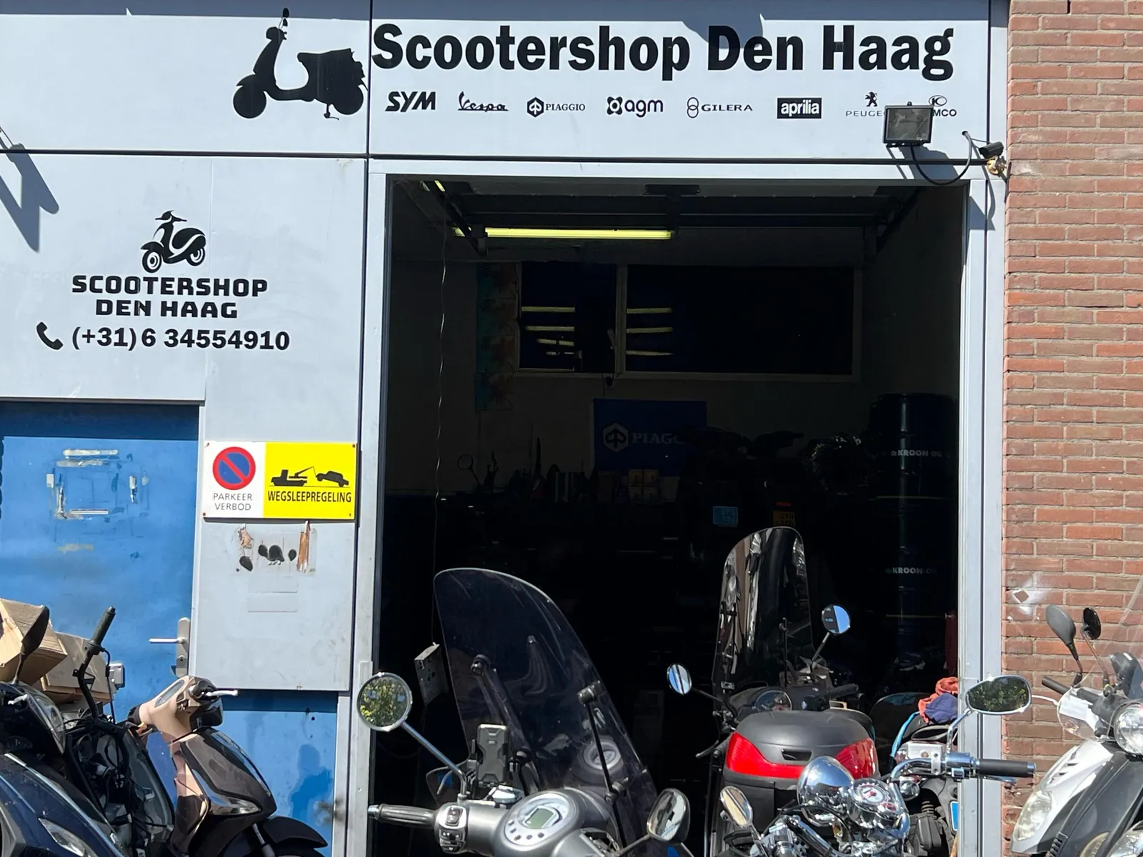 De werkplaats van Scootershop Den Haag aan de Marktweg, met de roldeur open en scooters voor de deur